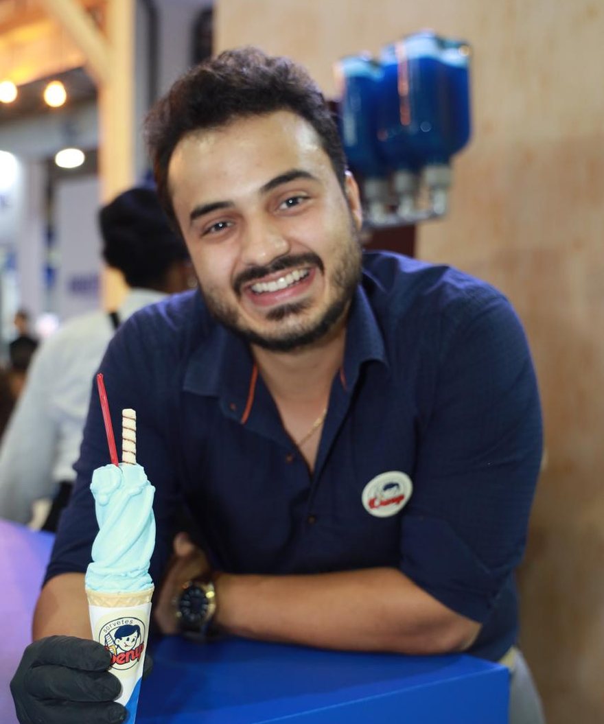 Denys Filho, fundador da Denys Sorvetes, atrás do balcão com uma casquinha da marca na mão