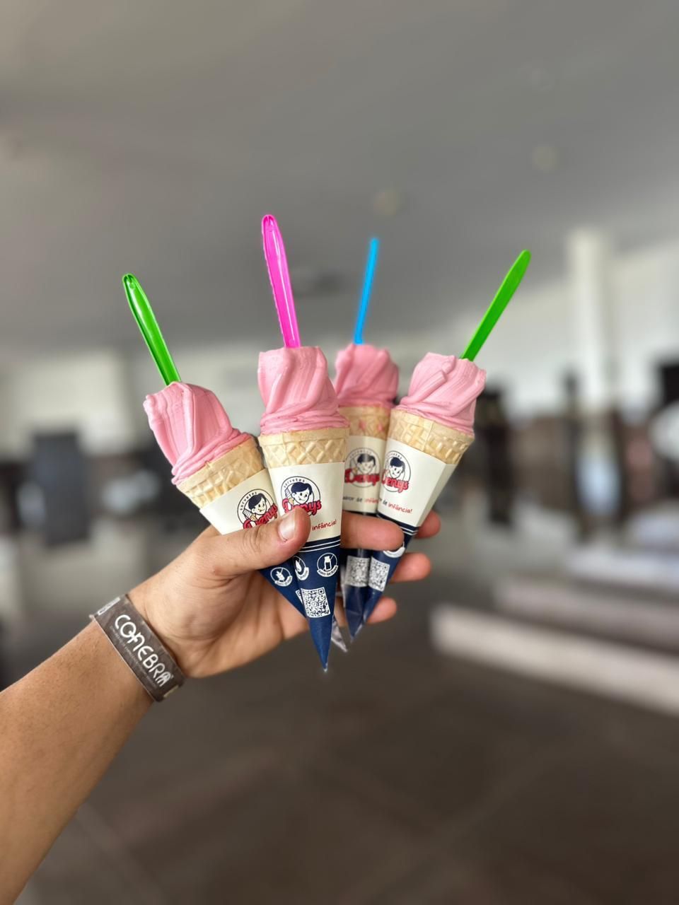Quatro casquinhas Denys de sorvete rosa seguradas na mão